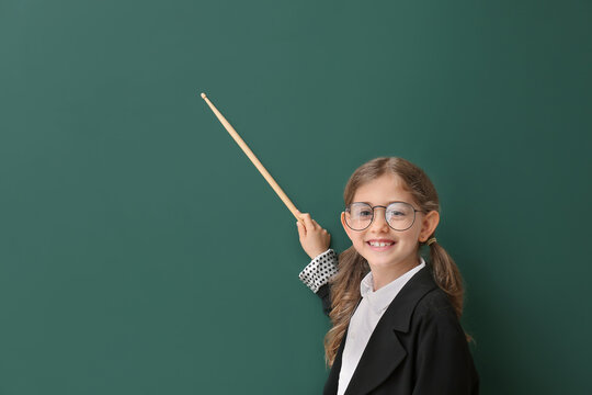 Cute little schoolgirl with pointer near blackboard in classroom