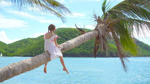 Adorable little girl at tropical beach on palm tree during summer vacation