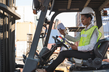 Black foreman woman worker driving forklift checking at Container cargo harbor to loading containers and has a problem. © Nopphon