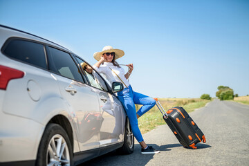 Pretty girl with suitcase standing near car and wiat for her dreaming trip. - obrazy, fototapety, plakaty