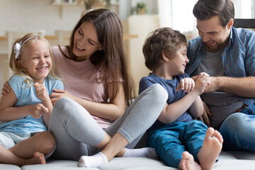 Happy young parents have fun play tickle with overjoyed little preschooler children, smiling mother...