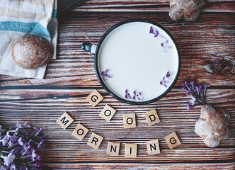 metal Cup with milk, homemade cookies and fresh branches of blooming lilac on a wooden table with the inscription of small wooden letters good morning, matte natural still life, content for blog