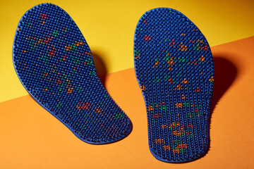 Blue massage insole for feet, with metal needles, spikes, on a yellow-orange background. For relaxation, health. Advertising, thematic and subject shooting.