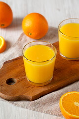 Healthy Orange Juice on a rustic board on a white wooden table, side view.