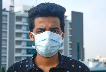 Portrait of young man wearing surgical face mask on a background of corporate company.corona virus, quarantine.