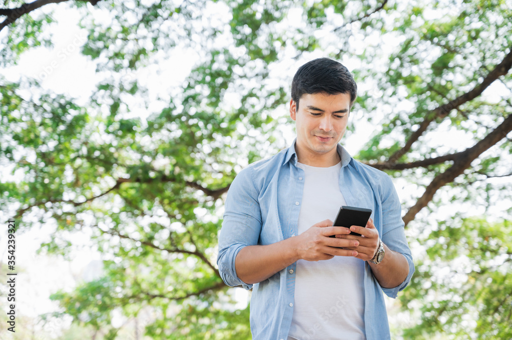 Wall mural young businessman caucasian, white using smartphone while walking in the park.