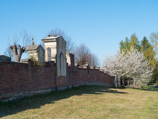 Fototapeta na wymiar old red brick wall of country cemetery at village Cvikov in luzicke hory, Lusatian Mountains, spring trees, blue sky