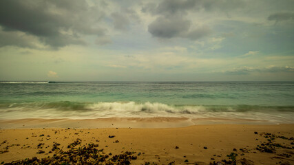 Beautiful seascape. Beach during daylight. Sandy beach with seaweeds. Waves captured with slow shutter speed. Cloudy weather. Bingin beach, Bali, Indonesia