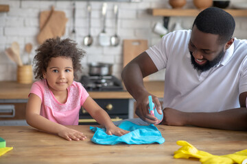 African american bearded man spraying disinfector on the table surface and his kid wiping