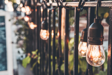 Trendy soft warm bulbs garland decoration on the metal fence. Street view, city retail and...