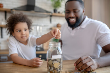 Cute curly-haired kid putting coins into the moneybank