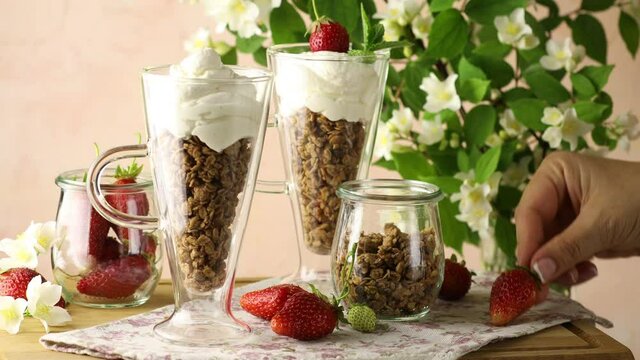 Woman hand decorated healthy breakfast with granola and greek yogurt fresh raw strawberry and fresh mint.