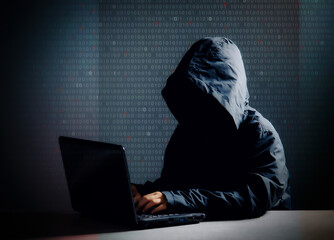 Internet crime concept,Hooded hacker using laptop in dark room