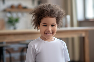 Cute curly-haired kid in a white tshirt smiling nicely