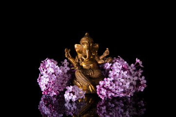 Hindu God Ganesha framed by pink lilac flowers on a black background with reflection