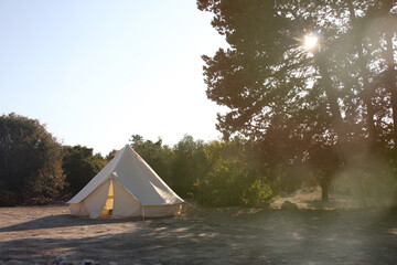 Glamping campsite in the forest at sunset. Big camping tent for luxury outdoor vacation. Staycations, hyper-local travel, night camping out concept. Copy space.