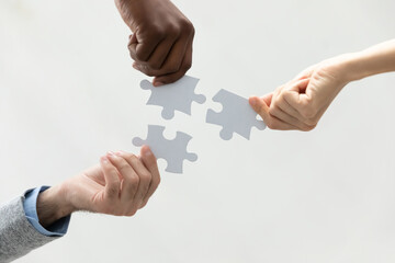 Close up bottom view diverse colleagues holding white pieces of puzzle, finding searching business...
