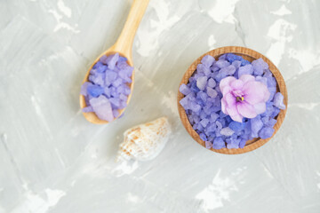 Bath salt and violet flowers on grey background, spa treatment, top view.