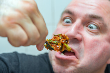 A crazy man with bulging eyes looks at fatty and junk food, sending it into his mouth. The concept of obesity and eating.