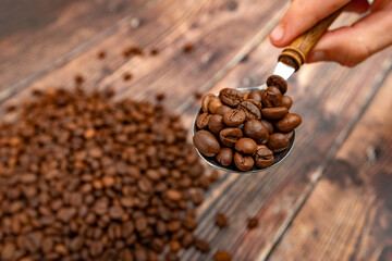 Roasted coffee grains in a spoon on a wooden background.