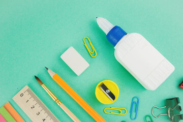 School supplies, top view of scissors, paper, watercolour paintings, brush, pen and ruler on the green background