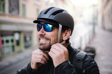 Delivery man courier fastening bicycle helmet and sunglasses in town.