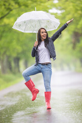 Pretty girl shows off in the rain holding a vintage umbrella, wearing red polka dot rain boots