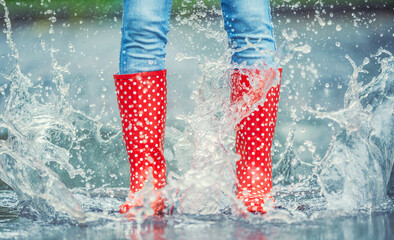 Detail of a moment when red polka dot rain boots jumped into a puddle of water, splashing all around