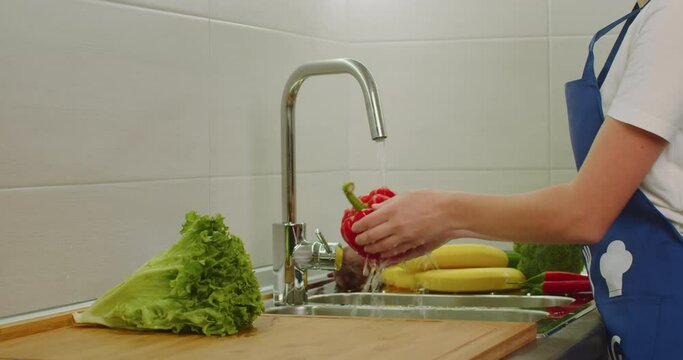 Close-up shooting. Women's hands are washing a large red pepper in the washbasin. Vegetables for salad. Shooting from the side. 4k