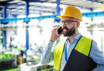 Fototapeta na wymiar Technician or engineer with hard hat standing in industrial factory, using telephone.