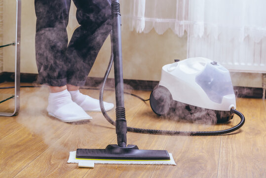 The woman washes the floor in the room with a white steam cleaner, a wet high-pressure steam. Cleaning of the apartment. we kill microbes. purity and order