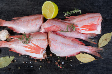 Raw redfish carcasses among the spices on black surface closeup