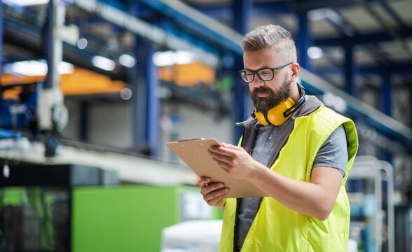 Technician or engineer with protective headphones standing in industrial factory.