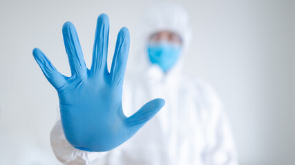 Doctor or physician in personal protective equipment (PPE) suit putting on surgical sterile gloves in hospital clinic. Blue rubber hand of medical worker. Preventing Coronavirus (COVID-19) infection.