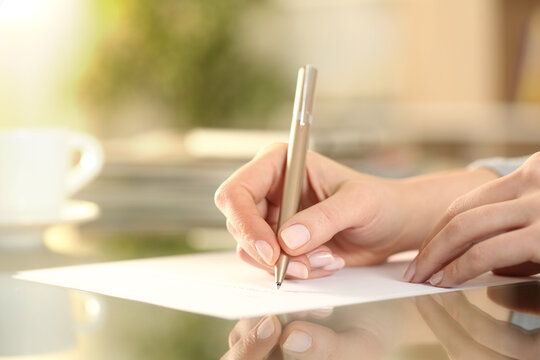 Woman hand writing on a paper on a desk at home