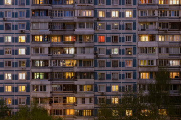 Fototapeta na wymiar Facade of large multi-storey block residential buildinf with many bright lighting windows in apartments and balconiesю Evening view. Moscow Russia