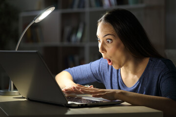 Amazed woman checking laptop at night at home
