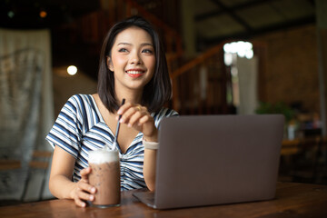 woman works at laptop in a cafe, woman's fingers typing on the keyboard. Workplace in a cafe, a cup of coffee next to a laptop, toned bright sunny photo