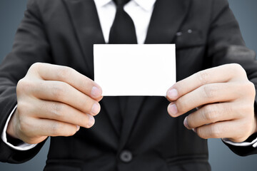 Closeup of businessman showing white piece of paper in black suit. Idea for business credit card or visiting card.
