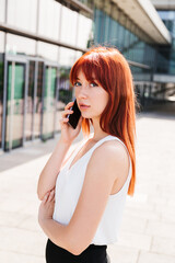 Fototapeta premium Red-haired girl talks on phone and looks at camera