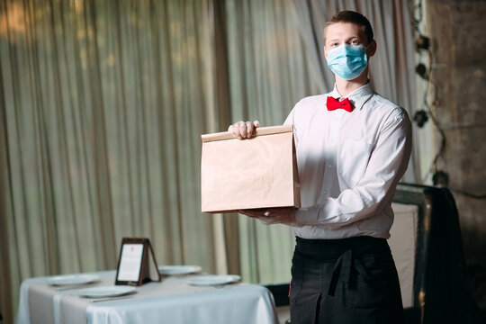 Food Delivery From The Restaurant. Portrait Of A Waiter Holding A Craft Paper Bag For Food Delivery.