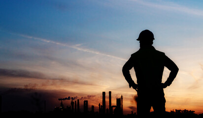 Rear view of silhouette engineer standing outdoors by oil refinery at dusk.