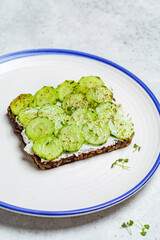 Cucumber and cream cheese toast on white plate, top view. Healthy vegetarian diet concept.