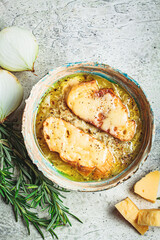 French traditional onion soup with baguette and cheese in gray ceramic bowl, top view.