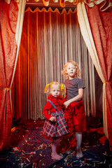 Two young girl sisters during stylized theatrical circus photo shoot in beautiful red location, Two...