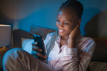 happy African American millennial woman as social media addict - night lifestyle portrait of young beautiful and cool black girl texting or online dating on mobile phone in bed