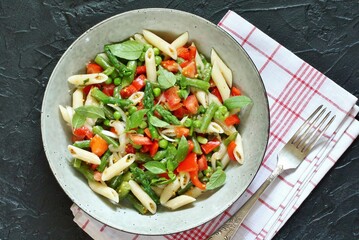 salad in a bowl of pasta, asparagus, bean pods, tomatoes, green peas, basil. top view, copy space