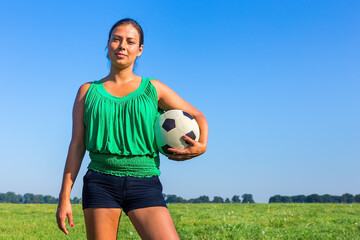 Standing young woman holds football outside
