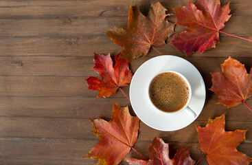 Cup of black coffee , maroon autumn maple leaves on a brown wooden background top view
