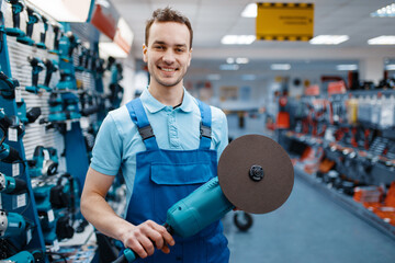 Male worker holds angle grinder in tool store